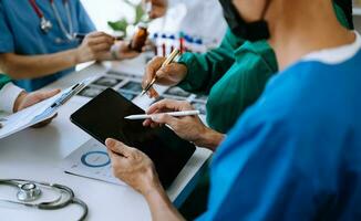 Medical team having a meeting with doctors in white lab coats and surgical scrubs seated at a table discussing a patients working online using computers photo