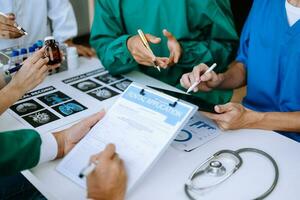 Medical team having a meeting with doctors in white lab coats and surgical scrubs seated at a table discussing a patients working online using computers photo