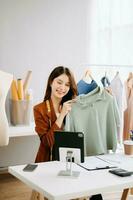 Fashion blogger concept, Young Asian women selling clothes on video streaming.Startup small business SME, using smartphone or tablet taking receive and checking photo