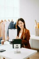 Asian tailor woman working on clothes in tailoring atelier.  beautiful young female fashion designer smile and after success in studio photo