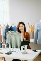Fashion blogger concept, Young Asian women selling clothes on video streaming.Startup small business SME, using smartphone or tablet taking receive and checking photo