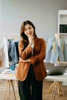 asiático Sastre mujer trabajando en ropa en sastrería taller. hermosa joven hembra Moda diseñador sonrisa y después éxito en moderno estudio foto