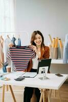 Moda blogger concepto, joven asiático mujer de venta ropa en vídeo streaming.startup pequeño negocio pequeño, utilizando teléfono inteligente o tableta tomando recibir y comprobación foto