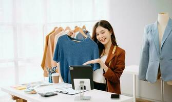 Fashion blogger concept, Young Asian women selling clothes on video streaming.Startup small business SME, using smartphone or tablet taking receive and checking photo