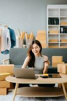 Startup small business SME, Entrepreneur owner woman using smartphone or tablet taking receive and checking online purchase shopping order to preparing pack product box. photo