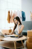Startup small business SME, Entrepreneur owner woman using smartphone or tablet taking receive and checking online purchase shopping order to preparing pack product box. photo