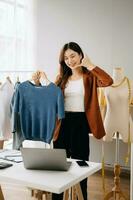 Asian young woman on desk in office of fashion designer and holds tablet, laptop and smartphone on white table photo