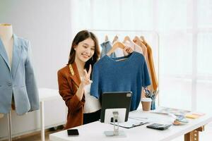 Fashion blogger concept, Young Asian women selling clothes on video streaming.Startup small business SME, using smartphone or tablet taking receive and checking photo