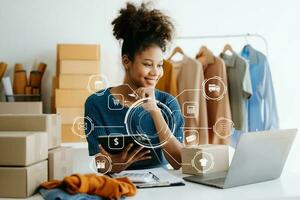 African Woman using a laptop, smartphone and tablet and writing notebook at the modern office of her business online shopping. In home with virtual icon photo