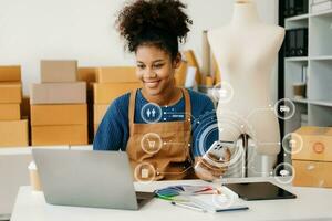 africano mujer utilizando un computadora portátil, teléfono inteligente y tableta y escritura cuaderno a el moderno oficina de su negocio en línea compras. en hogar con virtual icono foto