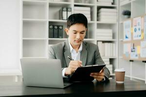 Young business man working at office with laptop, tablet and taking notes on the paper. photo