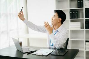 Happy asian businessman have the joy of talking on the smartphone, tablet and laptopon the office photo