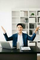 Young real estate agent worker working with laptop and tablet at table in modern office and small house beside it. photo