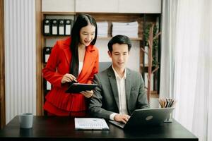 Two Asian businesswoman discuss investment project working and planning strategy with tablet laptop computer in  office. photo