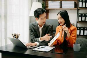 Two Asian businesswoman discuss investment project working and planning strategy with tablet laptop computer in  office. photo