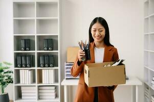 Happy and excited young beautiful Asian woman office worker celebrating her resignation, carrying her personal stuff. leaving job, changing or company.in office photo