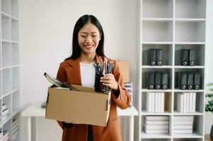 Happy and excited young beautiful Asian woman office worker celebrating her resignation, carrying her personal stuff. leaving job, changing or company.in office photo