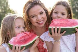 portrait of mom with cute daughters have fun while eating a slice of watermelon photo