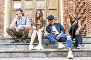 group of multiracial friends sitting on a marble staircase using smartphones photo