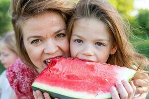 portrait of mom with cute daughters have fun while eating a slice of watermelon photo