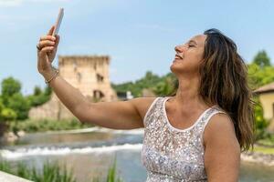 beautiful middle aged woman takes a selfie in front of an ancient tower of italian castle photo