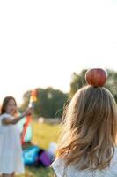 linda pequeño niña es jugando con un juguete arco y flecha con su hermana foto