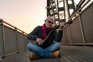 attractive middle aged musician man playing an electric violin outdoors photo
