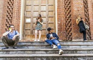 group of multiracial friends sitting on a marble staircase using smartphones photo