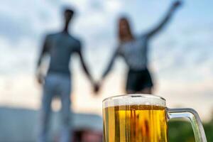 close-up of a glass of beer in front of a multiracial couple of lovers blurred in the background photo