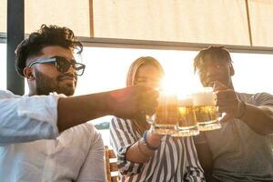 small group of young adult multiethnic friends toasting with three mugs of beer photo