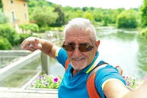 hermoso medio Envejecido hombre con blanco barbas de chivo tomando un selfie en el calles de un italiano pueblo por el lago foto