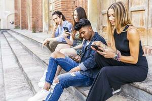 group of multiracial friends sitting on a marble staircase using smartphones photo