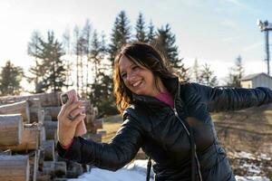 middle aged woman wearing winter clothes taking a selfie over a mountain photo