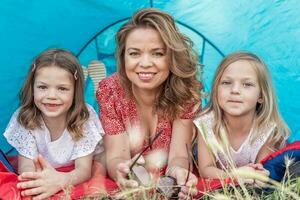 retrato de linda rubia mamá con su hijas acostado abajo en un azul cámping tienda foto