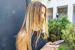 Portrait of blonde young woman in front of a newsstand using smartphones photo