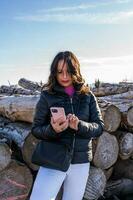 medio Envejecido mujer vistiendo invierno ropa utilizando inteligente teléfono en el nieve terminado un montaña foto