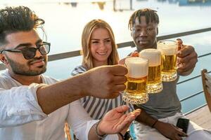 pequeño grupo de joven adulto multiétnico amigos tostado con Tres tazas de cerveza foto