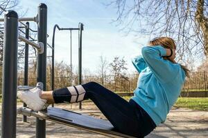 portrait of young woman doing abdominal muscles workout on a bench outdoors photo