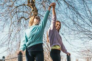 couple of female athletes having fun while climbing on sport metal structure outdoors photo