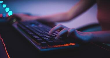 Footage close-up keyboard of Young Asian esport women gamers playing online video games on the computer with neon light at home. Girl gaming player feels enjoy technology broadcast live streaming.