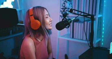 Aufnahmen von jung asiatisch Frau Influencer tragen Kopfhörer reden in ein Mikrofon während Aufzeichnung ein Radio Show im ein Leben Zimmer Zuhause Studio beim Nacht mit Neon- Licht. Inhalt Schöpfer Konzept. video
