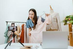 hermosa Asia mujer En Vivo transmisión de venta ropa en línea con teléfono inteligente a su tienda. pequeño negocio dueño, en línea mercado concepto. foto