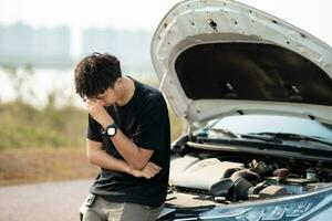 Worried asian young man stands in front of car checking condition after a broken car. Broken car down on the road. emergency service has broken car. photo