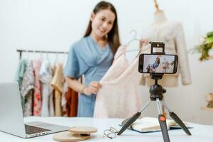 Beautiful Asia woman Live streaming selling clothes online with smartphone at her shop. Small business owner, online market concept. photo