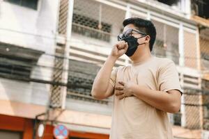 Asian young man wearing face mask to protect PM 2.5, protect pollution, anti smog and viruses on road in the city. Global warming concept. Healthcare concept. Environmental pollution concept. photo