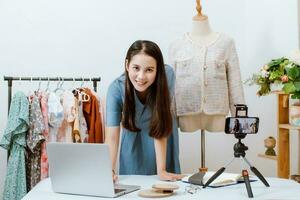 hermosa Asia mujer En Vivo transmisión de venta ropa en línea con teléfono inteligente a su tienda. pequeño negocio dueño, en línea mercado concepto. foto