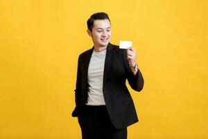 Young Asian man shows his credit card on a yellow background. photo