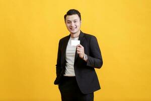 Young Asian man shows his credit card on a yellow background. photo