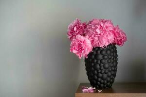 The peony or paeony pink flowers in vase at the shelf. Paeonia Sarah Bernhardt bouquet on grey background. Home interior concept photo