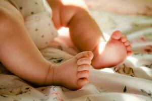 recién nacido bebé niña en el cuna. niños pequeños piernas en el cama. dos mes caucásico infantil en el pañal. pequeño babys pies y dedos foto